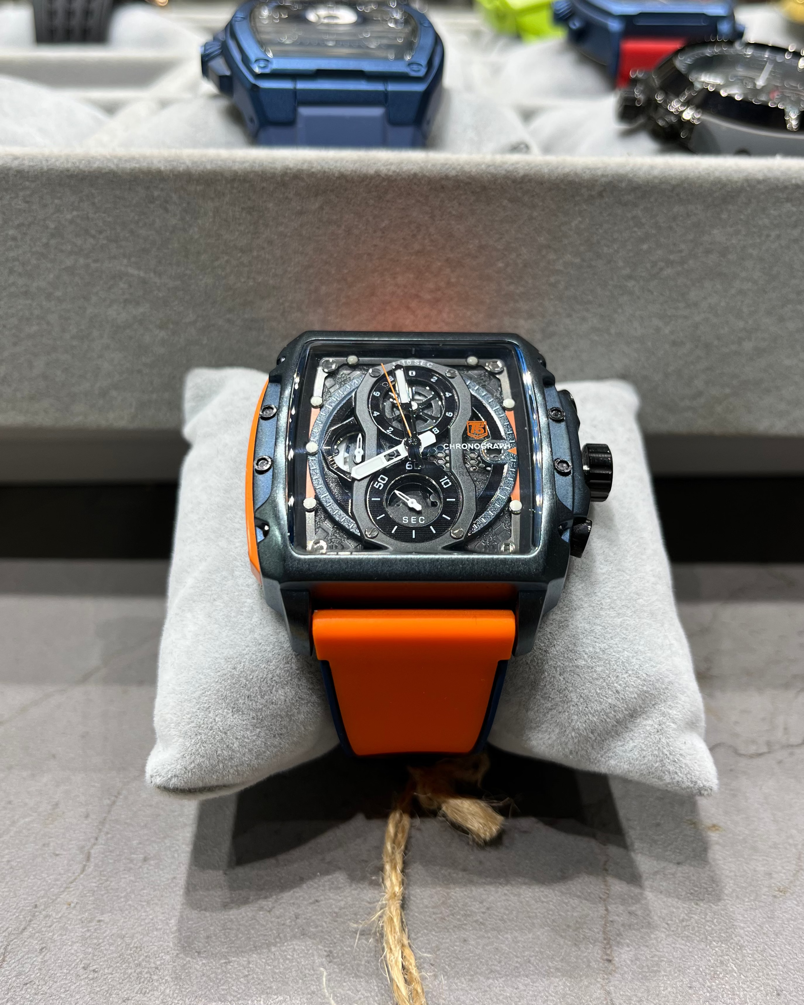 Watch with orange strap on a gray surface, with other watches in the background