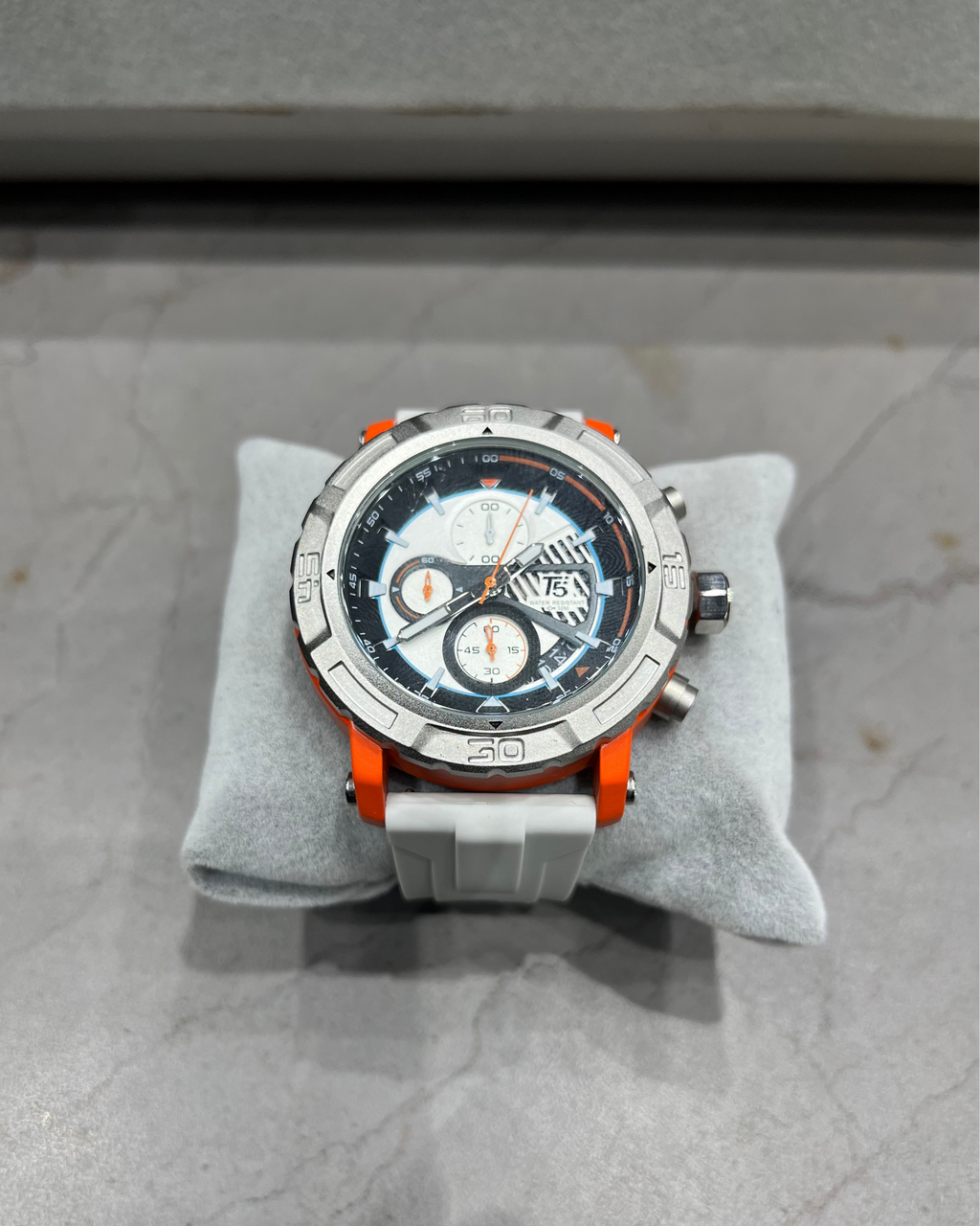 Wristwatch with orange accents on a gray cushion against a gray background
