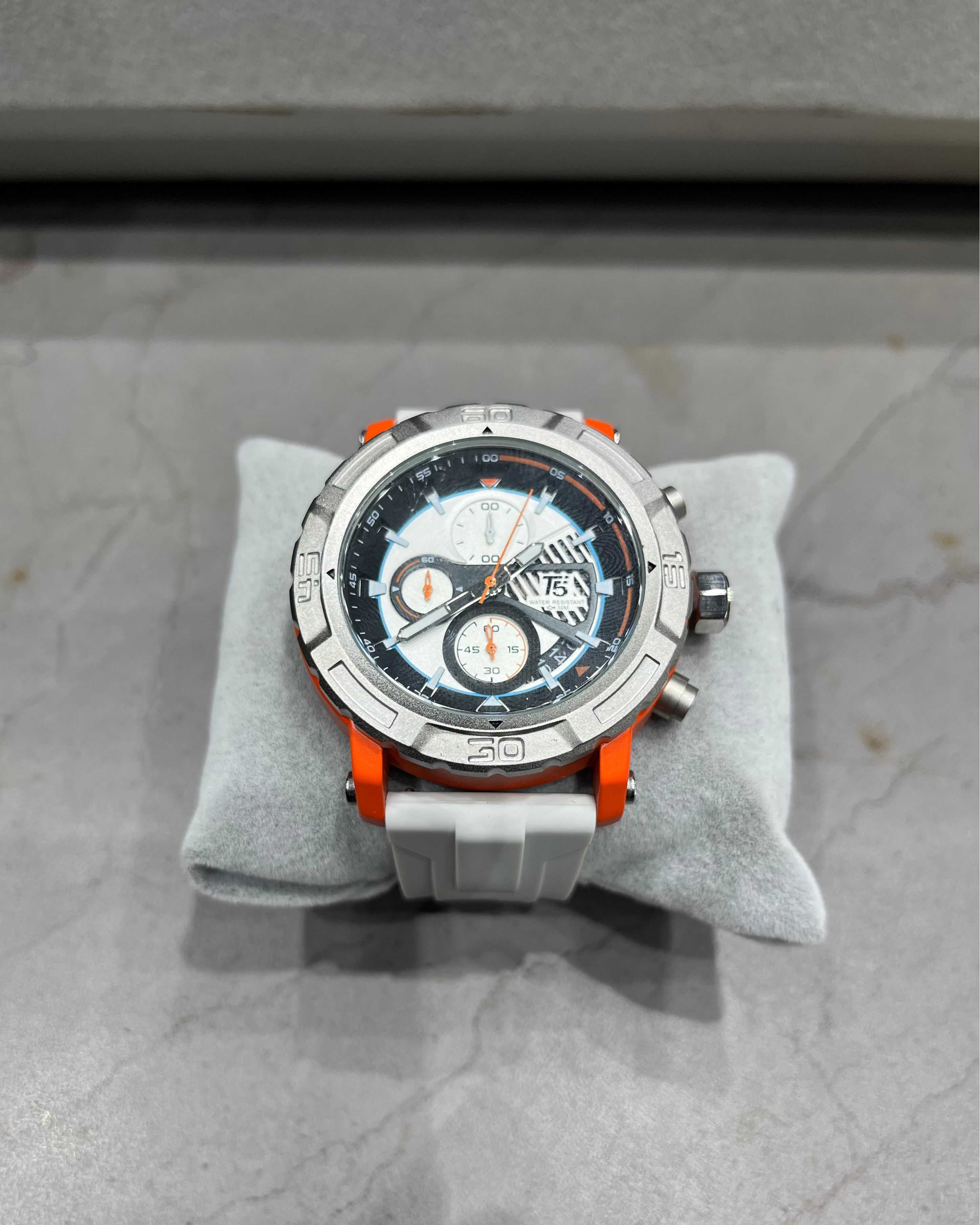 Wristwatch with orange accents on a gray cushion against a gray background