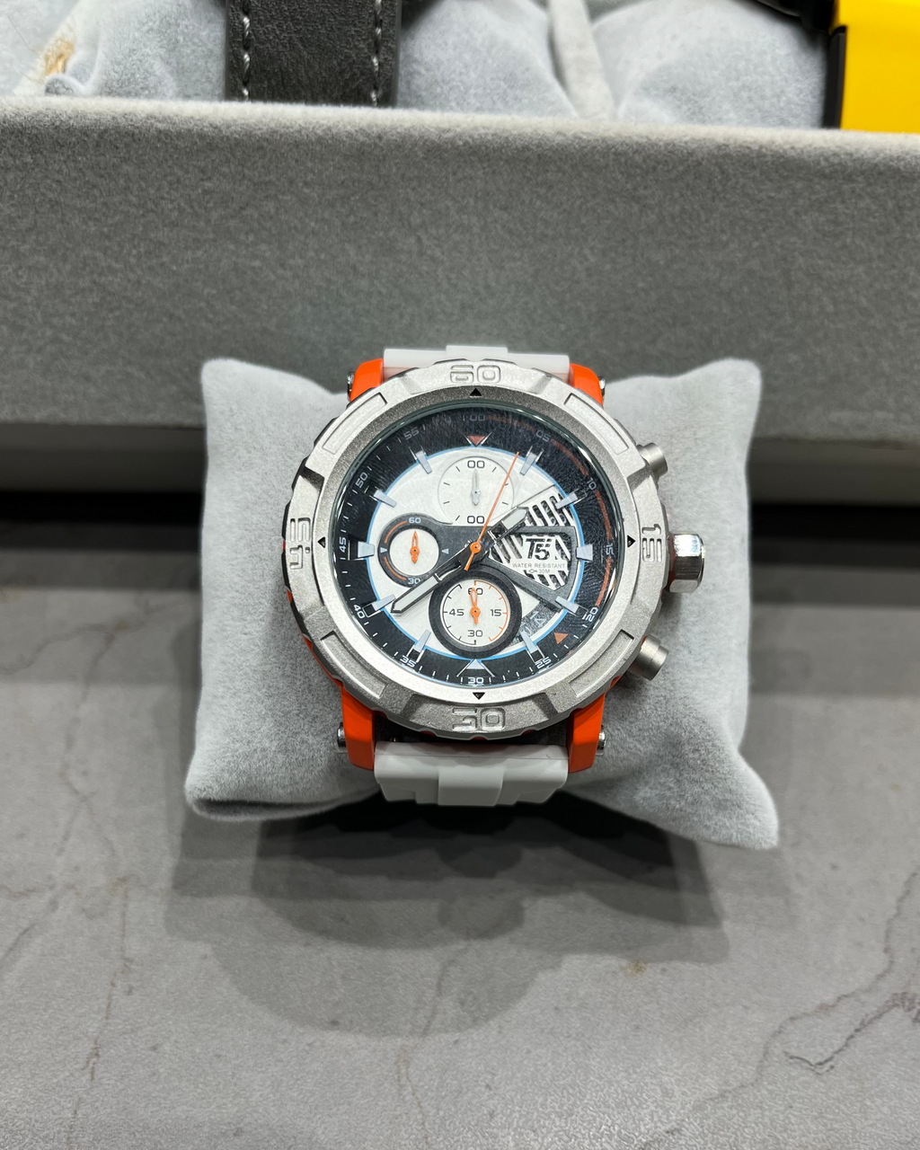 Watch with a detailed face on a gray cushion, likely in a store setting