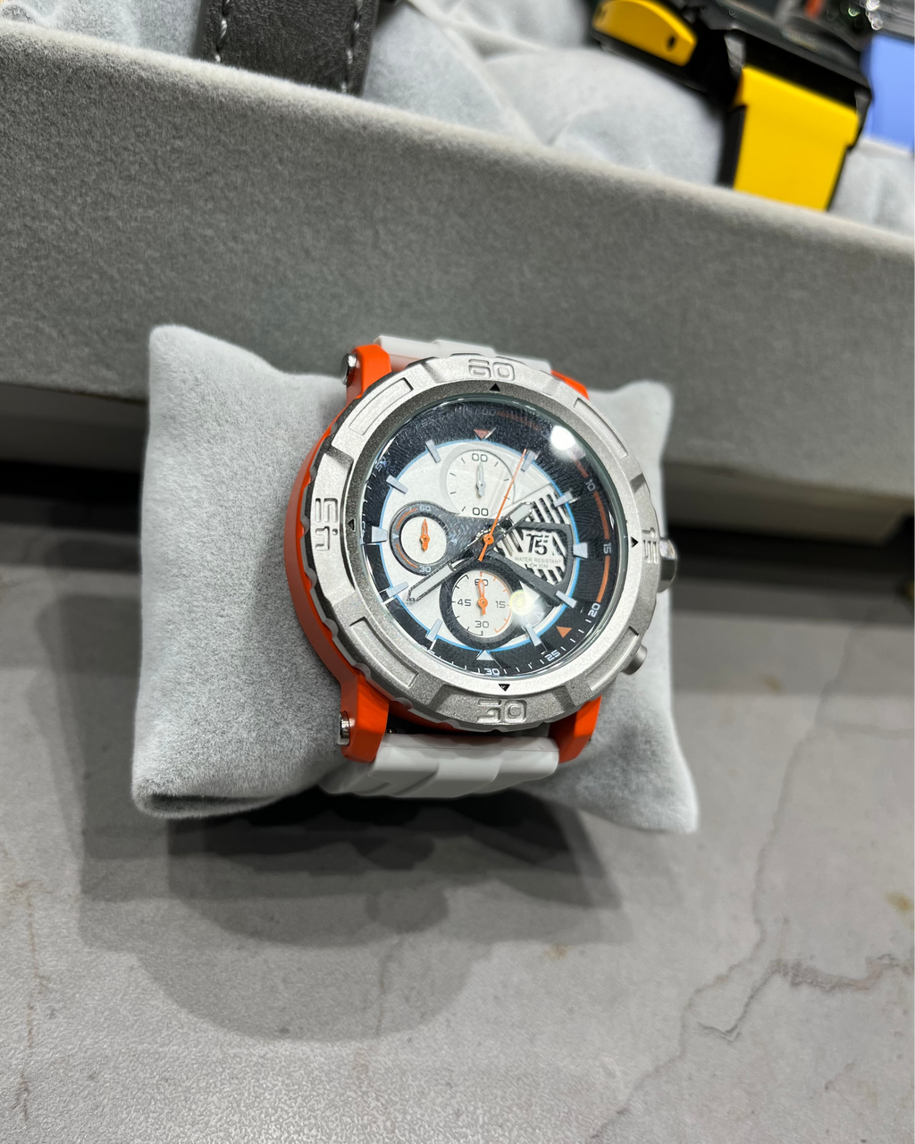 Wristwatch with orange accents on a gray cushion, with a blurred background