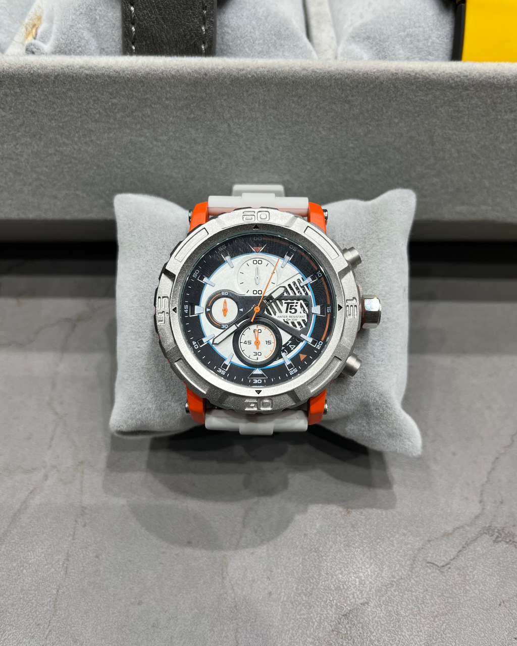 Wristwatch with a detailed face on a gray cushion, likely in a display case.